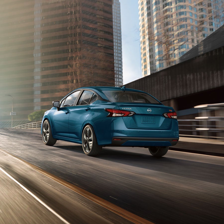 2025 Nissan Versa driving down a city highway with tall skyscrapers in the background